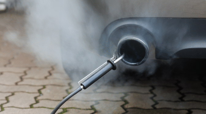 Car exhaust with visible fumes and test equipment attached